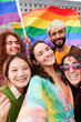 © Gigi Delgado - Happy vertical selfie of a group of LGBTQIA people in the pride day, looking at camera cheerfully holding rainbow flags. Concept of Supporting the Homosexual community.