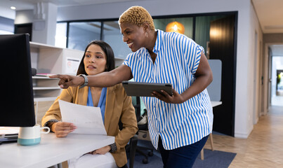 At office, diverse team member pointing at screen, holding business papers