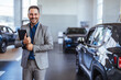 Cropped portrait of a handsome young male car salesman working on the showroom floor. Happy salesperson standing in a car showroom looking at camera.
