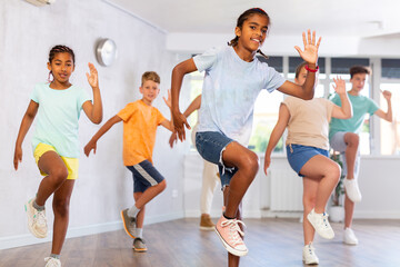 Wall Mural - Smiling african american preteen boy dancer practicing active vigorous dance with group in modern studio..