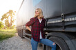 Confident woman truck driver in shirt and jeans posing next to the truck 