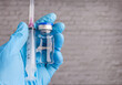 A gloved hand holds a vaccine bottle and syringe, representing medical or scientific procedures.