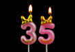 Burning pink birthday candles with gold bow and word happy isolated on black background, number 35.