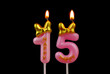 Burning pink birthday candles with gold bow and word happy isolated on black background, number 15.