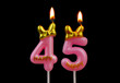 Burning pink birthday candles with gold bow and word happy isolated on black background, number 45.