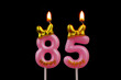 Burning pink birthday candles with gold bow and word happy isolated on black background, number 85.