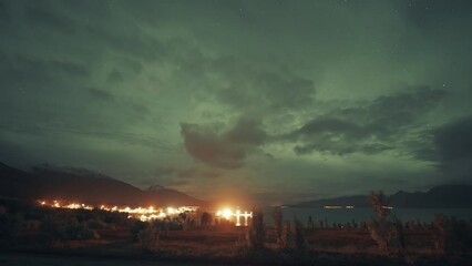Wall Mural - Aurora borealis in the cloudy sky above a brightly lit town and port in Northern Norway.
