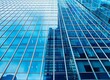 © graphito - Close up of a modern glass building facade with blue windows, a business center visible in the city background