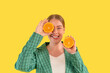 enjoying curvy woman with toothy smile covering eye with piece of orange on yellow background. concept of diet and healthy lifestyle	