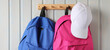 blue and pink school backpacks and a white baseball cap hang on a wooden hanger, close-up. Education, school and training.
