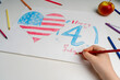 The American flag in the form of a heart is drawn by the child's hand with a red pencil. The Fourth of July is America's Independence Day. The concept of patriotic education.
