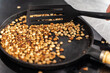 Coffee beans are roasted in a cast-iron pan. Green grains are mixed with a spatula. Selected focus.