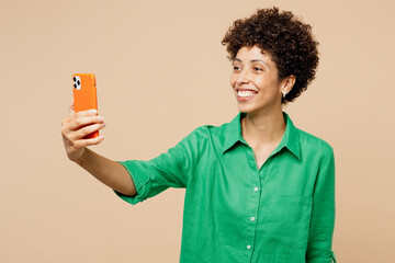 Wall Mural - Young woman of African American ethnicity wear green shirt casual clothes do selfie shot on mobile cell phone post photo on social network isolated on plain pastel beige background. Lifestyle concept.