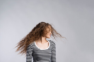 Wall Mural - Portrait of a gorgeous teenage girl with curly hair, blowing in wind. Studio shot, white background with copy space