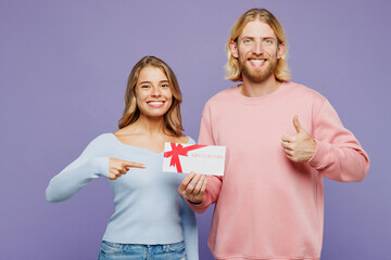 Wall Mural - Young fun couple two friends family man woman wear pink blue casual clothes together hold gift certificate coupon voucher card for store show thumb up isolated on pastel plain light purple background.