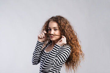 Canvas Print - Portrait of a gorgeous teenage girl with curly hair, holding lock of hair as a moustache. Studio shot, white background with copy space