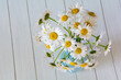Bouquet of beautiful chamomile flowers in a vase on a white wooden background