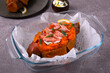 Baked stuffed sweet potato with hot smoked trout, sour cream sauce and topped with green onion in the glass dish