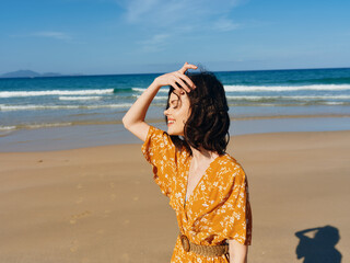 Poster - Woman in yellow dress enjoying the sunshine and fresh ocean breeze on sandy beach, standing with hands on head