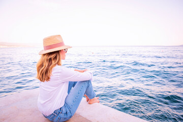 Wall Mural - Rear view of a middle-aged woman sitting on the pier and enjoying the view of the sea