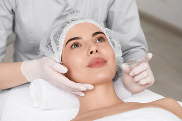 Canvas Print - Professional cosmetologist holding skincare ampoule while working with client in clinic, closeup