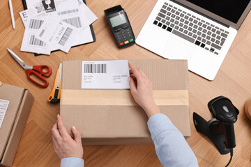 Poster - Parcel packing. Post office worker sticking barcode on box at wooden table, top view