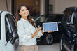 © Dragana Gordic - Picture of professional female salesperson working in car dealership. Young well dressed sales woman standing in car dealership saloon with tablet.