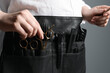 Hairstylist with professional tools in waist pouch on grey background, closeup