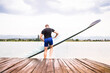 Young canoeist putting canoe into water, standing on wooden dock. Concept of canoeing as dynamic and adventurous sport