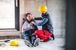 Colleague giving first aid to injured worker, in pain after accident at construction site Concept of occupational safety and health in workplace.