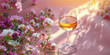 A wine glass filled with golden wine sits amidst pink flowers, bathed in warm sunset light.