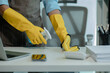 a cleaner is wiping everything in office with towel and sanitizer spray to remove all dust, wearing gloves to protect hands from chemical that use to cleanup all object for hygiene