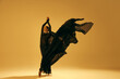 © master1305 - Freedom and inspiration. Young female ballet dancer wearing black flowing costume and dancing against sand color background. Concept of art, classical dance, beauty and fashion, aesthetics