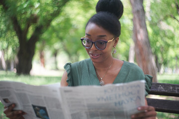 Beautiful and young black woman reading a newspaper in the park