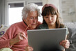 Grandmother with cute girl scrolling on tablet, girl teaching senior woman to work with technology, internet. Portrait of elderly woman spending time with granddaughter.