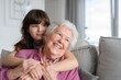 Cute girl hugging gradmother from behind. Portrait of an elderly woman spending time with granddaughter.