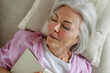 Top view of beautiful mature woman asleep with book. Weekend activity for older woman, relaxing at home.