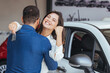 Finally we bought a car. Happy young couple chooses and buying a new car for the family in the dealership. Smiling couple hugging and holding their new key at new car showroom