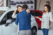 Happy couple embracing after receiving keys from their new car in a showroom. Yay honey, we have bought a new car! Happy couple buying a car at the dealership and holding the keys