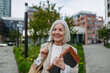 Mature businesswoman scrolling on smartphone, going home from work. Beautiful older woman with gray hair walking down city street.