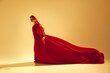 © master1305 - Power and grace. Elegant woman wearing flowing red dress and face accessories, performing against sand color background. Concept of art, classical dance, beauty and fashion, aesthetics