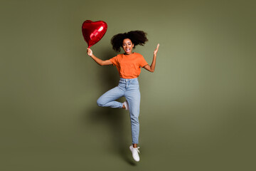 Sticker - Full length photo of impressed lady dressed orange t-shirt jumping high rising heart balloon empty space isolated khaki color background