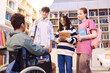 Diverse group of smiling teenage students talking to young boy using wheelchair in school library