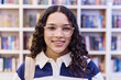 Close up portrait of teenage girl wearing glasses looking at camera in school library with bookshelves in background copy space