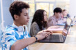 © Seventyfour - Side view portrait of Middle Eastern teenage boy using computer in library with diverse group of students in row copy space
