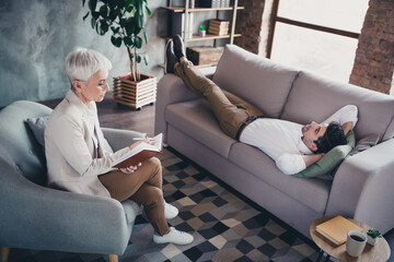 Canvas Print - Photo of young man lying couch visit consultation psychotherapist lady take notes loft interior office indoors