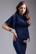 Portrait of young pretty pregnant woman on gray studio background. Female in blue sequin dress, hand on hip