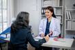 © apichat - A woman in a white lab coat is talking to a woman in a blue shirt