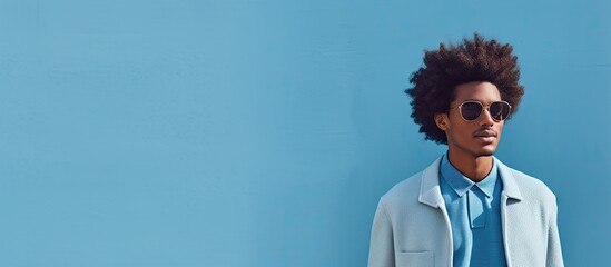 Wall Mural - A stylish young man with afro textured hair stands confidently in front of a blue wall with room for additional elements in the image