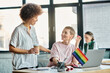 © Bliss - Cheerful diverse businesswomen working together on project in office, pride flag.